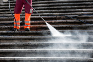 Man Pressure washing steps of commercial building